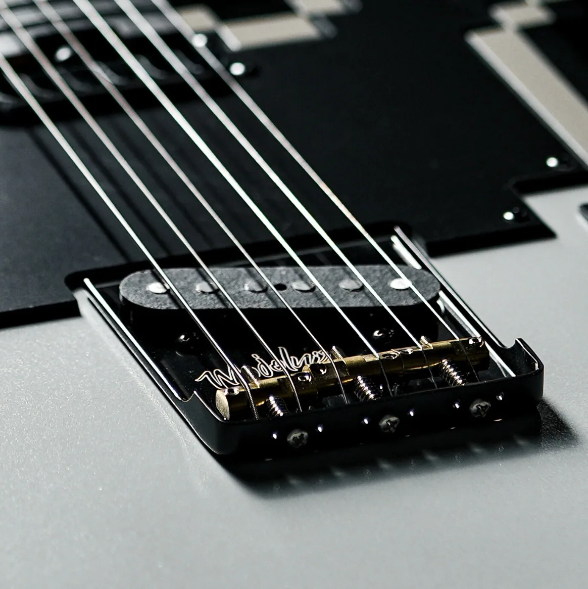 STAGE-T（BK）の固定式ブリッジ。斜めに並ぶ三つの真鍮サドルと「Mojolnir BY MOJO TEAM」の刻印